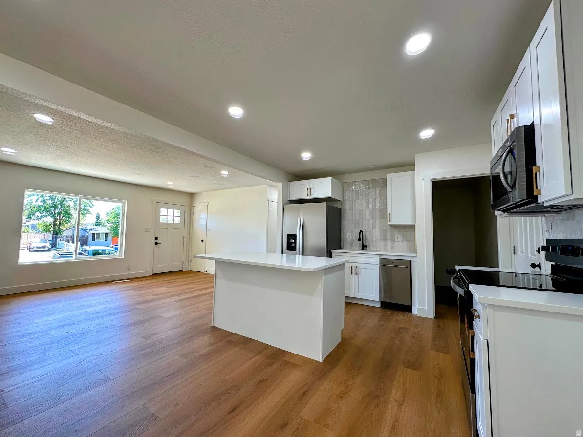 Open-concept living space with wood-finish flooring, white cabinetry, a kitchen island, and recessed lighting
