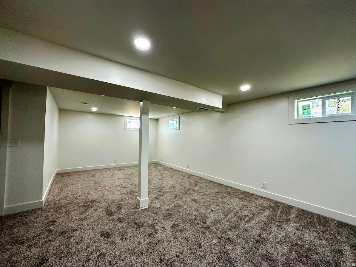 Spacious room with new carpeting, white painted walls, recessed lighting, and multiple windows