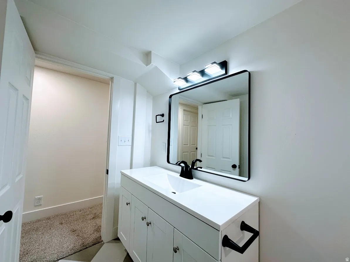 White vanity with integrated sink, black framed mirror, three-light vanity bar, and black fixtures