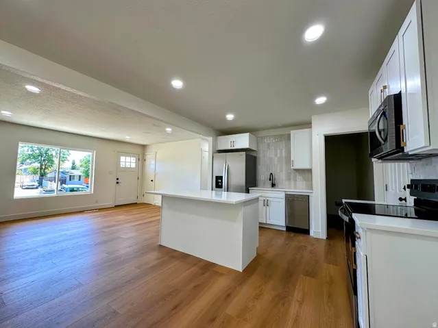 Open-concept living space with wood-finish flooring, white cabinetry, a kitchen island, and recessed lighting