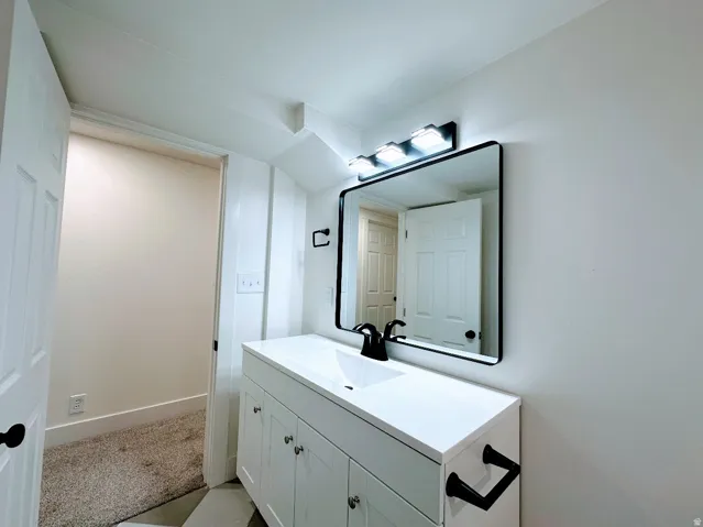 White vanity with integrated sink, black framed mirror, three-light vanity bar, and black fixtures