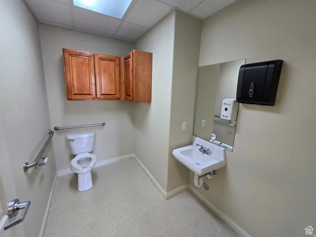 Restroom featuring a wall-mounted sink, mirror, toilet, and two stainless steel grab bars