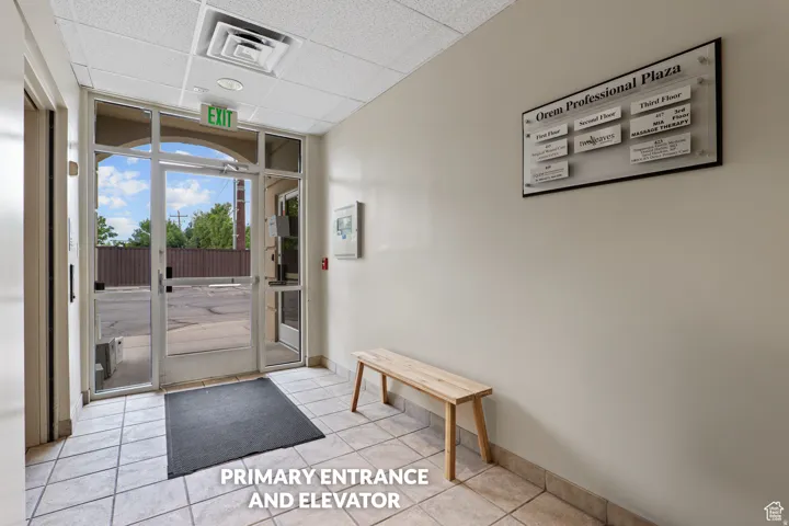 Tiled entryway with glass paneled doors and a dropped ceiling