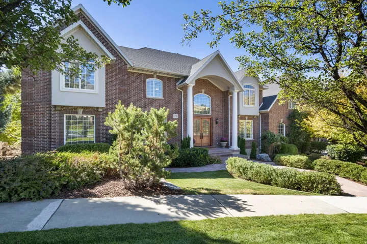 Brick facade with stucco accents, arched entryway, double wood doors, decorative columns, and mature landscaping