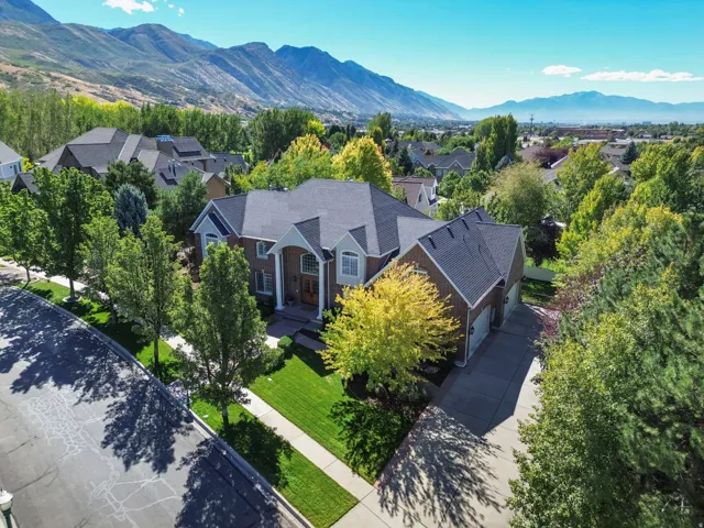 Expansive property featuring a brick exterior, prominent gabled rooflines, a multi-car driveway, mature trees, and a mountain backdrop