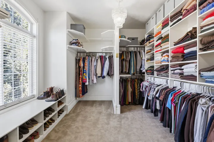 Walk-in closet featuring extensive built-in shelving, multiple hanging rods, and a window with blinds