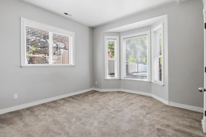 Neutral gray wall paint, white trim, bay window, carpeted flooring, and a single pane window