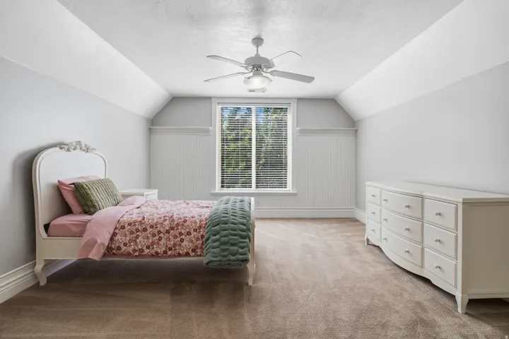 Window with blinds, wall paneling, ceiling fan with integrated lighting, and sloped ceiling
