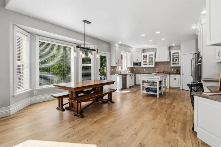 Open-concept kitchen and dining area featuring light wood-finish flooring, white cabinetry, a central island, and a bay window