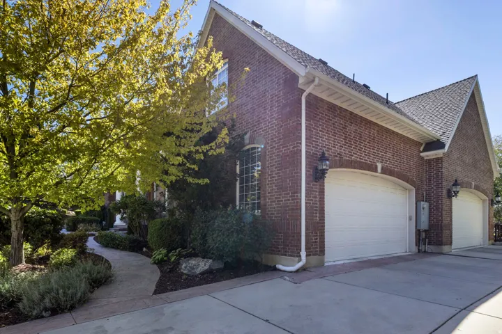 Brick exterior with arched garage doors, concrete driveway, stone walkway, and mature landscaping