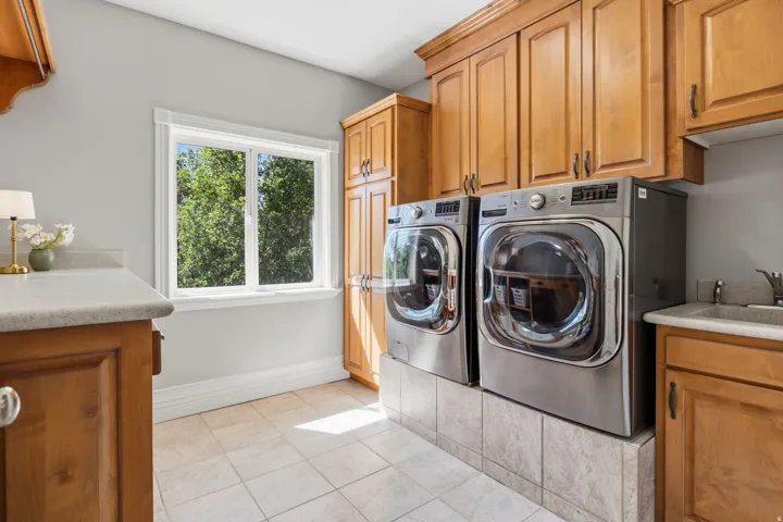 Laundry room featuring wood cabinetry, a utility sink, tiled flooring, and a large window