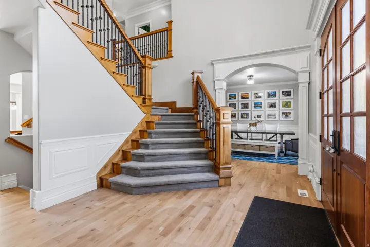 Hardwood flooring throughout the entry, a detailed staircase with wood treads and iron balusters, wainscoting, a decorative arched entryway, and a paneled wood-finish door with frosted glass inserts