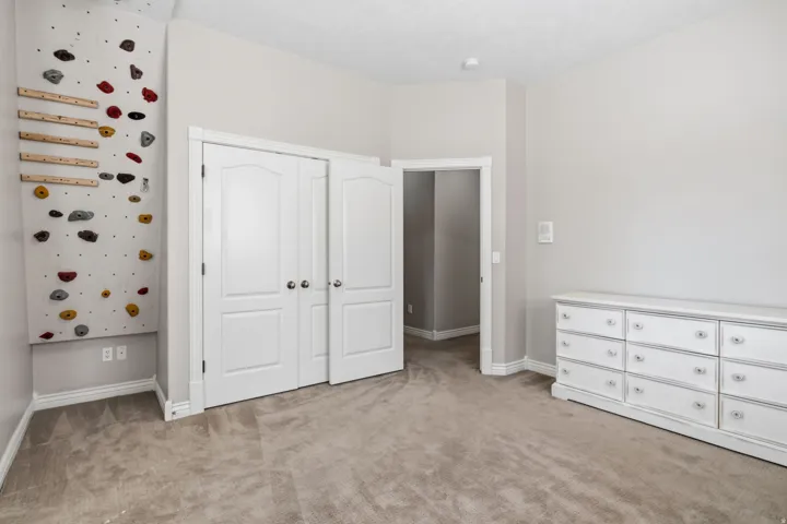 Wall-mounted climbing feature with varied grips, neutral gray walls, and light-colored carpeting