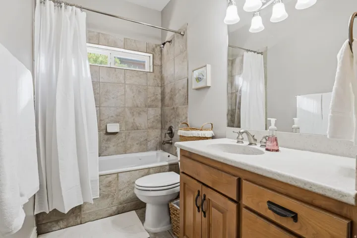 Tub-shower combination with tiled surround, wood-finish vanity with countertop, and an integrated sink
