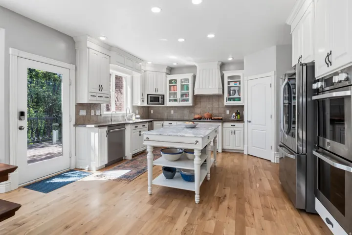 Kitchen featuring light wood-finish flooring, white cabinetry, a central island with a marble-finish countertop, and stainless steel appliances