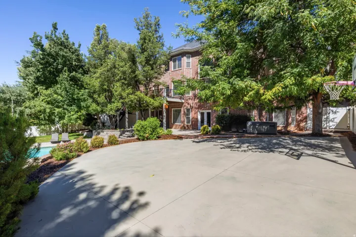Expansive concrete patio with mature trees, brick exterior, multiple exterior doors, and a swimming pool