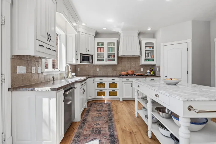 Kitchen featuring white cabinetry, wood-finish flooring, a stainless steel dishwasher, a built-in microwave, and an island with a light-colored stone countertop