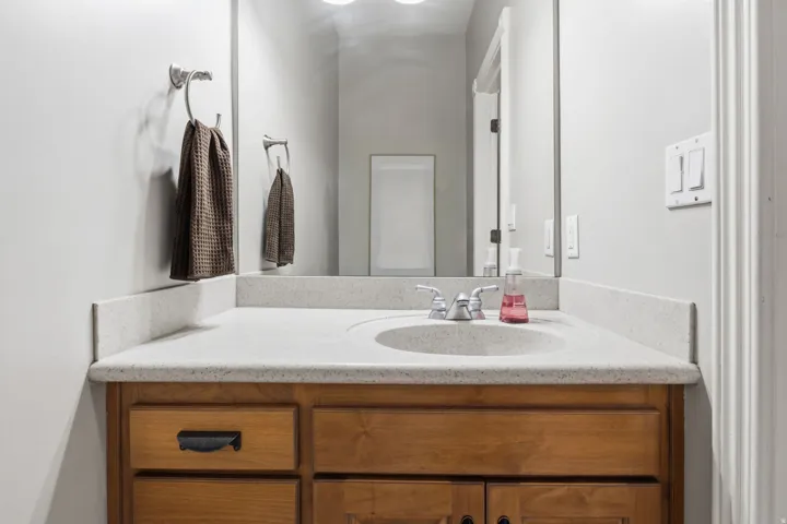 Bathroom vanity featuring a built-in sink with a polished chrome faucet, light-toned countertop, and wood-finish cabinetry with dark hardware