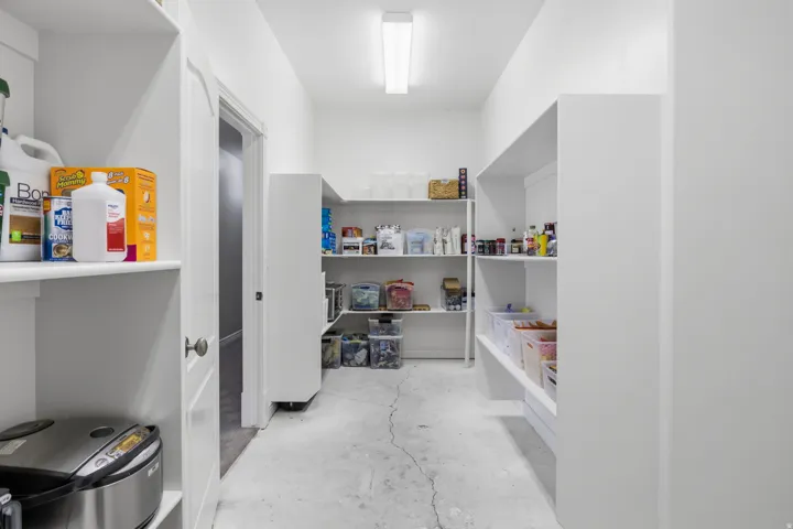 Walk-in pantry featuring extensive built-in shelving, white walls, and overhead lighting