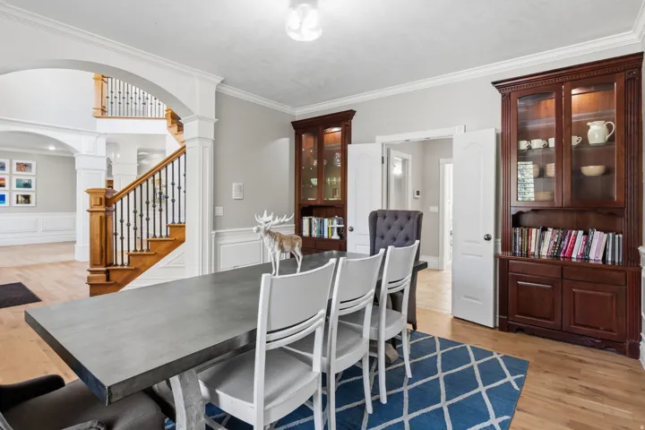Hardwood flooring, elegant wainscoting, solid wood staircase with wrought iron balusters, built-in display cabinets, and arched doorways