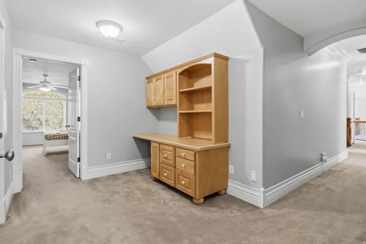 Built-in desk with overhead cabinetry and shelving, arched doorway, and light gray wall paint