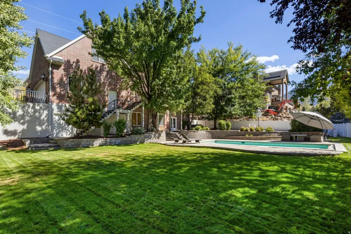Expansive lawn area with a rectangular swimming pool, bordered by mature trees and a brick exterior dwelling