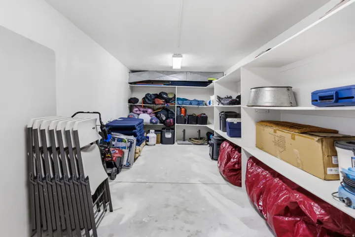 Spacious storage area featuring concrete flooring, built-in shelving, and white painted walls