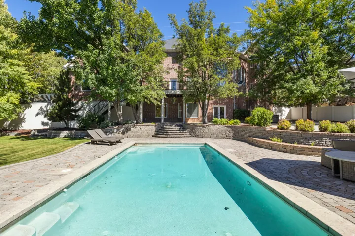 Expansive backyard featuring a rectangular swimming pool, paver patio, stone retaining walls, and mature trees