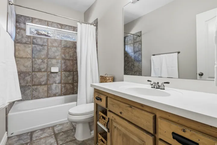 Bathtub with a tiled surround and transom window, wood-finish vanity with an integrated sink, and a large wall-mounted mirror