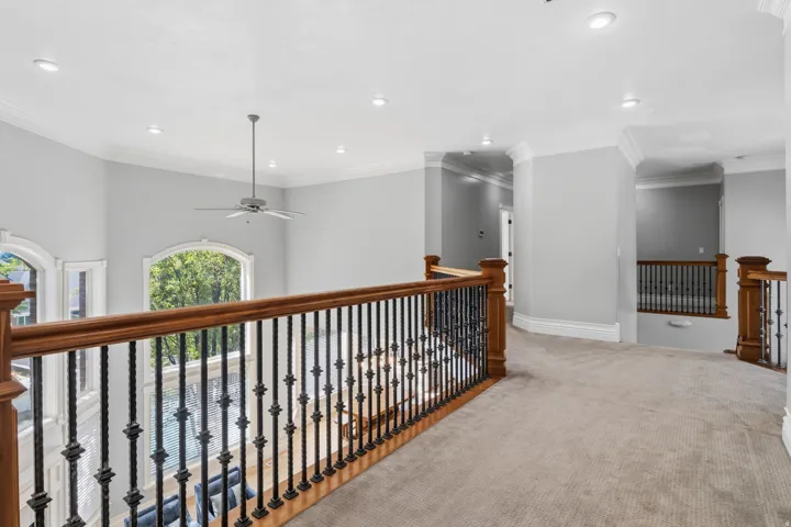 Spacious landing featuring carpet flooring, wood handrails with wrought iron balusters, recessed lighting, and crown molding