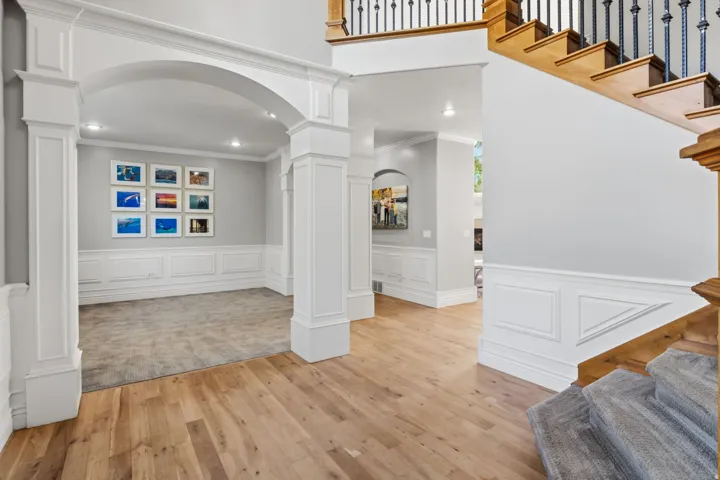 Hardwood flooring, arched entryway, wainscoting, recessed lighting, and a grand staircase with decorative balusters