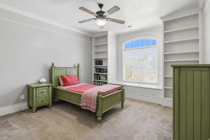 Arch-top window with blinds, flanked by built-in shelving, crown molding, and a ceiling fan