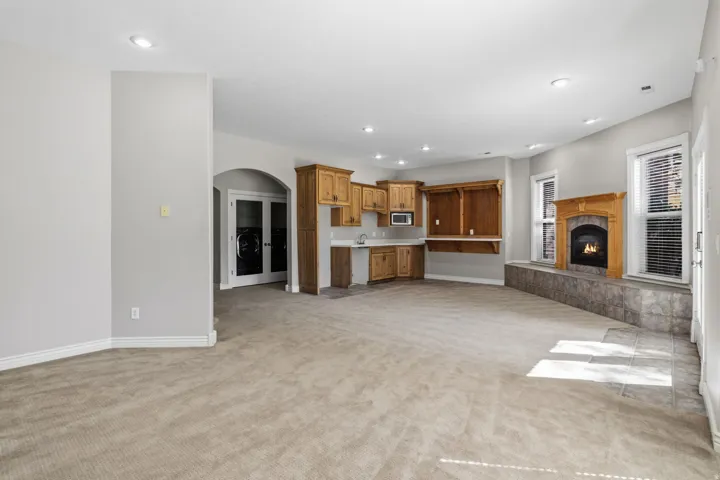 Recessed lighting illuminates this space featuring a built-in wet bar with wood cabinetry, a fireplace with a wood mantel, and an arched entryway