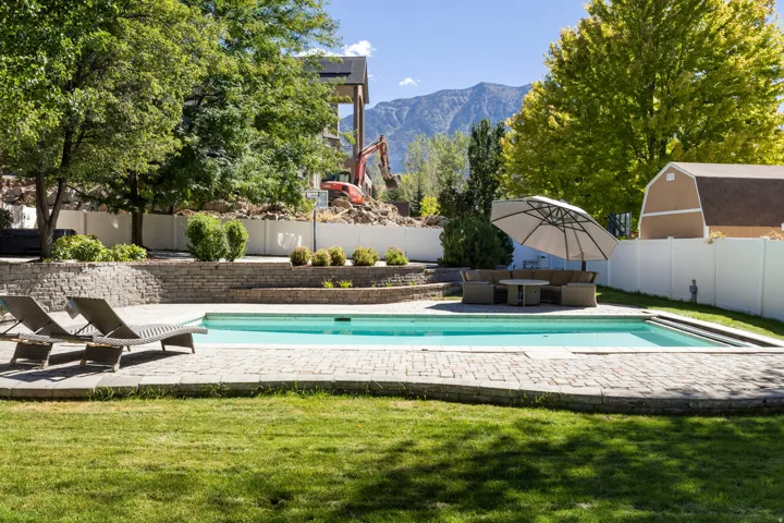 Expansive lawn area with a stone paver pool deck, a rectangular swimming pool, and tiered stone retaining walls