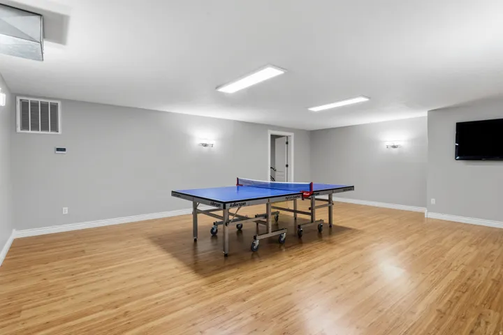 Spacious room featuring wood-finish flooring, recessed lighting, wall-mounted sconces, and a wall-mounted television