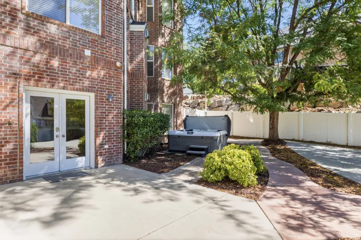 Brick exterior with white double doors, concrete patio, and a hot tub
