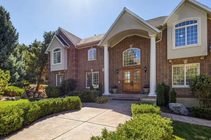Brick exterior featuring a portico with columns, arched entry, double wood doors, and a stamped concrete driveway