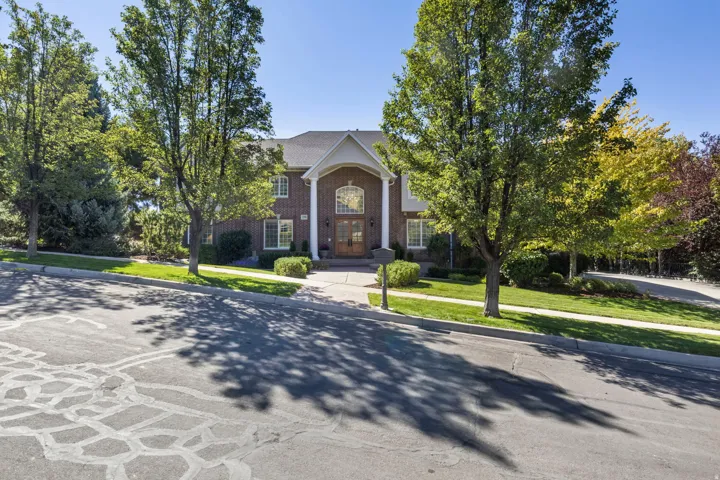 Brick facade with white trim, arched portico, column accents, mature trees, and a manicured lawn