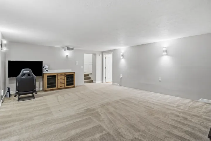 Expansive room featuring light-toned carpeting, wall-mounted sconces, and a built-in media cabinet with a light-toned countertop