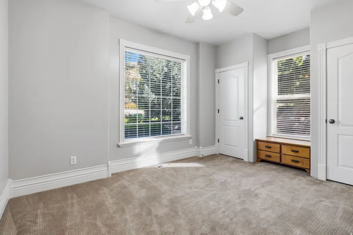 Plush carpet flooring, multiple windows with blinds, white trim, and a ceiling fan