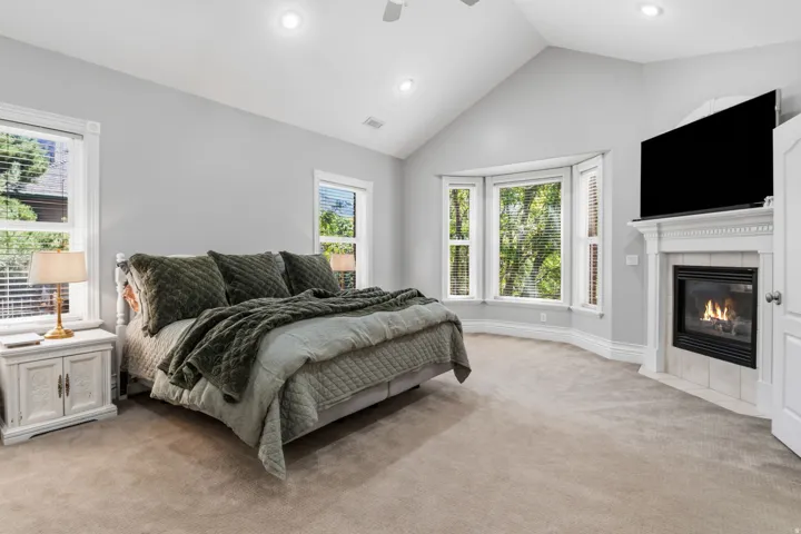 Vaulted ceiling with recessed lighting, bay window, wall-mounted fireplace with tile surround, and neutral carpeting