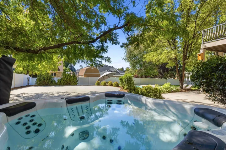 Integrated spa with multiple jets, concrete patio, mature trees, and privacy fencing