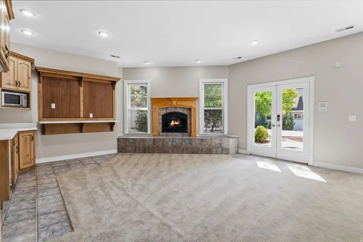 Built-in wood cabinetry with a microwave, a stone-clad fireplace with a wood mantel, dual pane windows, recessed lighting, and patio access via French doors