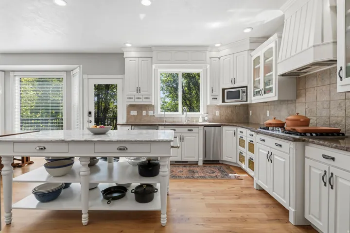 White cabinetry with crown molding, stainless steel appliances, wood-finish flooring, and a large center island with a marble countertop