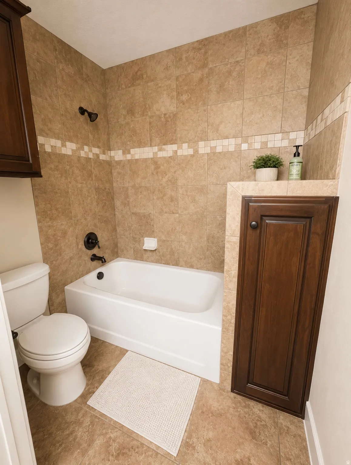 Full bathroom featuring a white bathtub with dark bronze fixtures, light brown tiled surround with decorative accent band, and a matching tiled floor