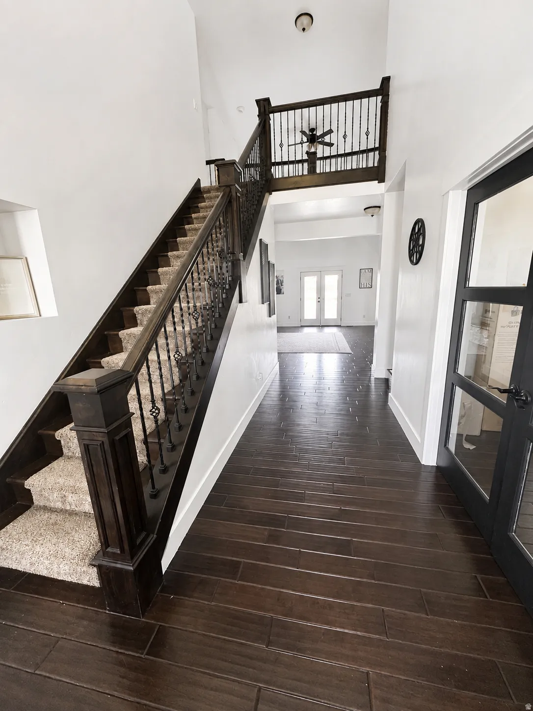 Two-story foyer with dark wood-finish flooring, a grand staircase featuring dark wood newel posts and wrought iron balusters, and a carpeted runner