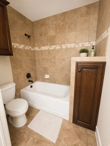 Full bathroom featuring a white bathtub with dark bronze fixtures, light brown tiled surround with decorative accent band, and a matching tiled floor