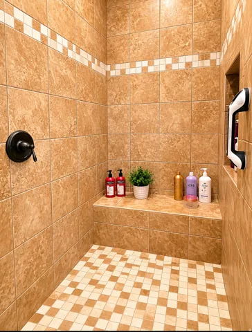 Tiled shower enclosure featuring a bronze-finish control knob, an integrated shower bench, a recessed wall niche, and a checkered mosaic tile floor
