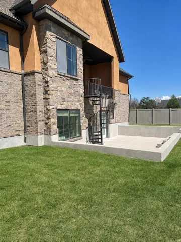 Exterior featuring stucco and stone veneer, with a built-in outdoor patio space, a spiral staircase, and a wood-look privacy fence
