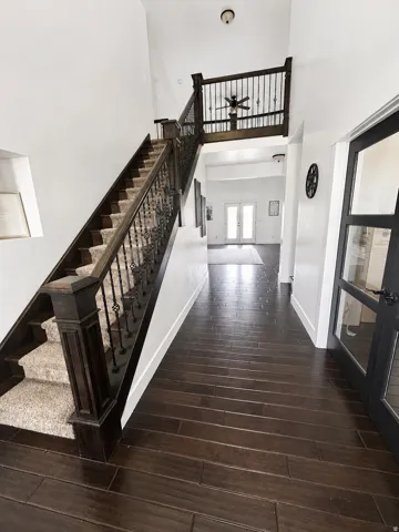 Two-story foyer with dark wood-finish flooring, a grand staircase featuring dark wood newel posts and wrought iron balusters, and a carpeted runner